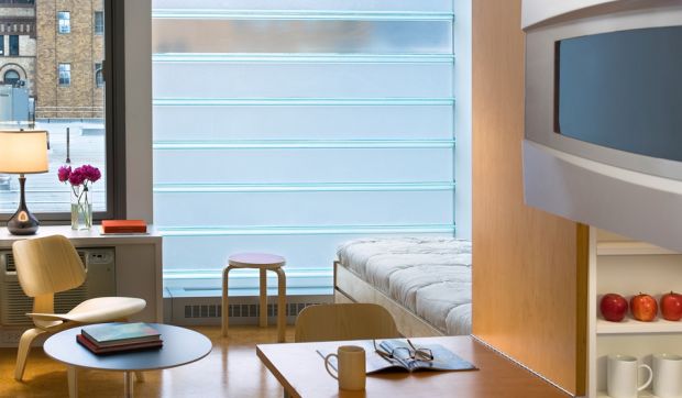 The interior of an apartment, with bed, desk, tables, and window looking out