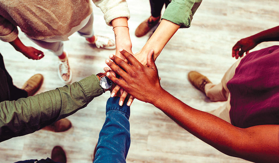 A diversity of people putting their hands on top of one another's in the center of a room.