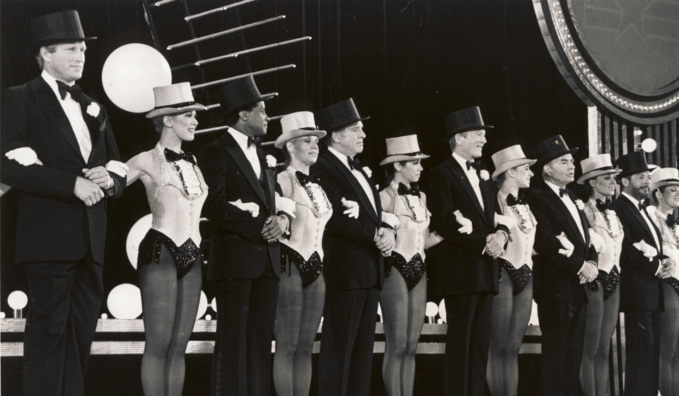 Men and women form a kickline at a performance.